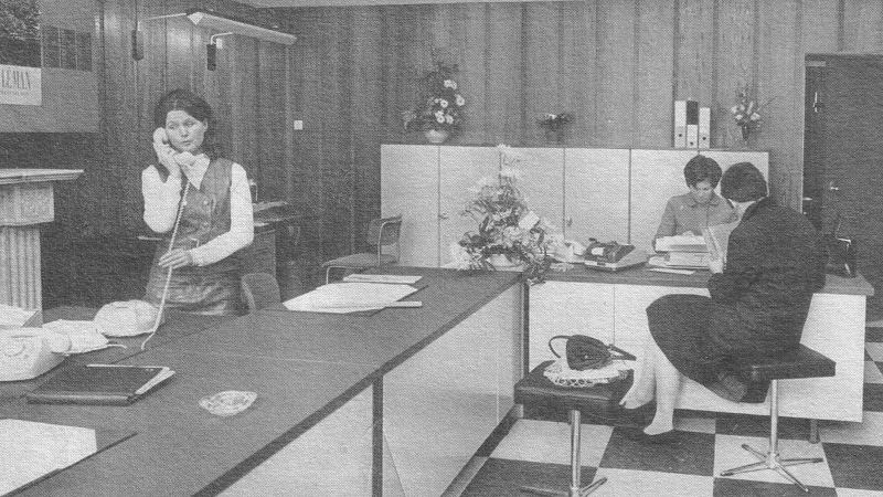 zwartwitfoto van de balie van het MAIC, links een telefonerende receptioniste