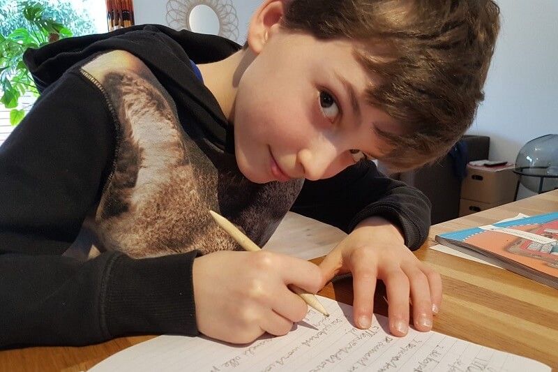 jongen van 10 jaar buigt voorover en schrijft in schoolschrift