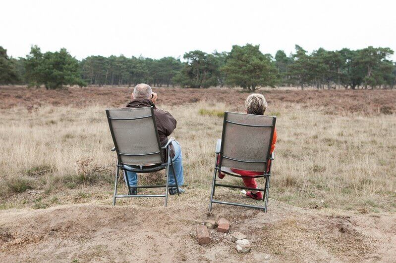 man en vrouw op campingstoel op de heide, man kijkt door verrekijker