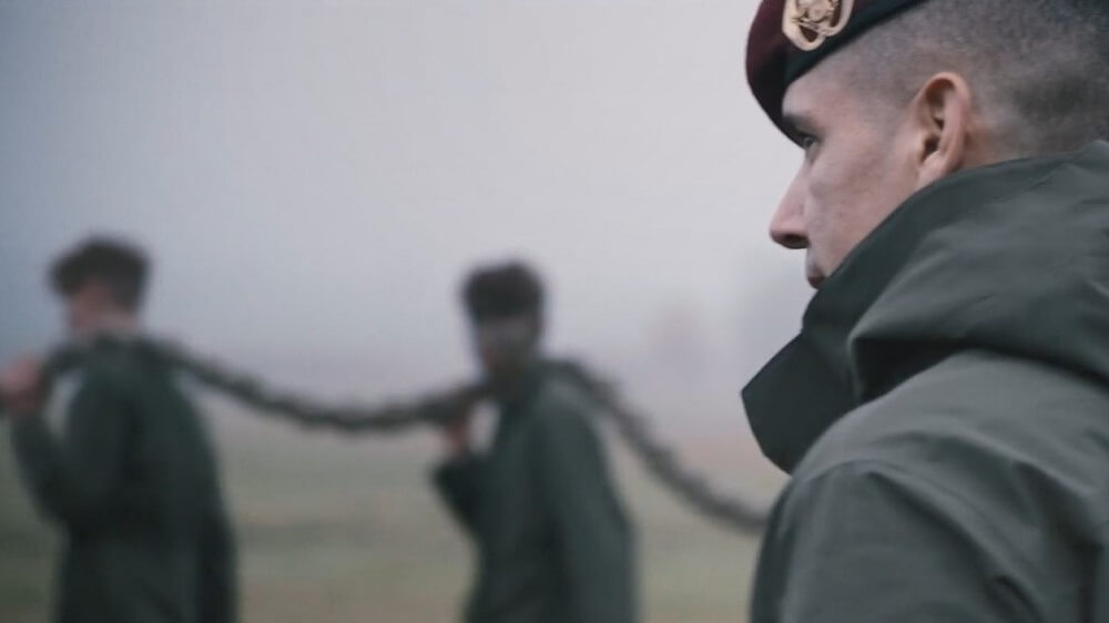 soldaat met baret kijkt naar links terwijl kadetten op de achtergrond trainen met een dik touw